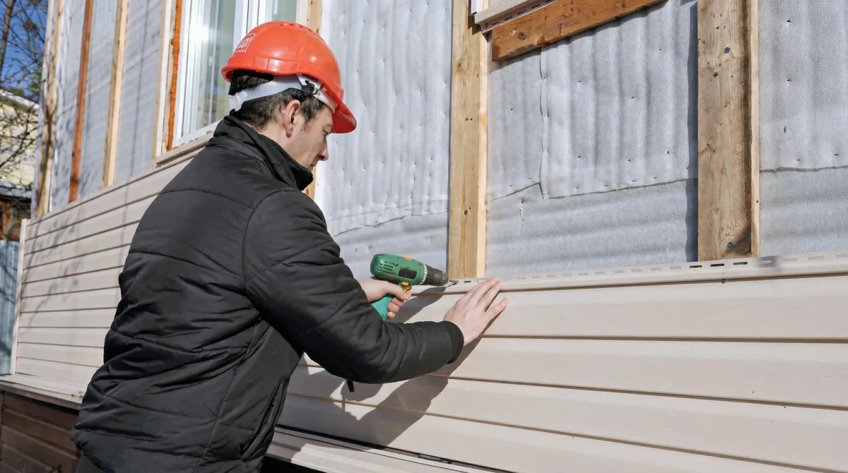 Siding replacement professional using a power drill to install new tan vinyl siding on a home exterior in Milwaukee, WI